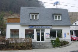 Kleines Autohaus mit Ford-Schildern, Treppe und rotem Auto rechts.
