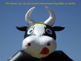 Aufblasbare Kuh mit großen Hörnern vor blauem Himmel; Text oben: Begrüßung auf Webseite.