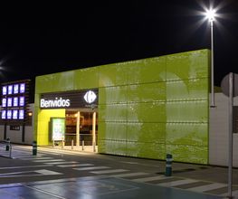 Entrada iluminada de supermercado Carrefour de noche con letrero que dice "Benvidos".