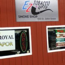 Smoke shop exterior with signs for EZ Tobacco Gifts, Royal Vapor, and an "Open" neon sign.