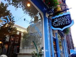 Blauw geschilderd café met bord "Stads Koffyhuis", weerspiegeling van bomen in het raam.