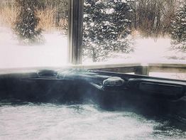 Steamy outdoor hot tub surrounded by snowy trees and landscape.