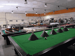 Sala con mesas de billar alineadas y lámparas colgantes. Ambiente iluminado y espacioso.
