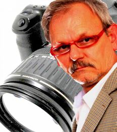 Eine Person mit roter Brille vor einer großen Kamera im Hintergrund.