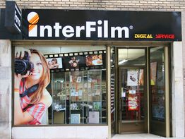 Fachada de tienda InterFilm con cartel de mujer sosteniendo cámara y fotos en la ventana.