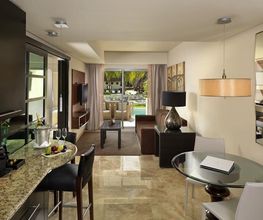 Sala moderna con cocina, mesa de vidrio y vista al balcón. Muebles elegantes y lámpara colgante.