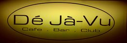Dekoratives Schild: "Dé Jà-Vu Cafe · Bar · Club" in einem ovalen Rahmen auf gelbem Hintergrund.