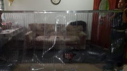 Un panel transparente se levanta delante de un sofá en una sala; dos personas lo sostienen.