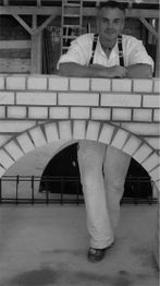 Ein Mann in Arbeitskleidung lehnt lächelnd an einer gemauerten Bogenstruktur.