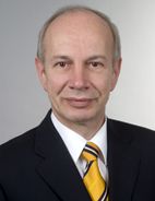 Person im Anzug mit gestreifter Krawatte vor grauem Hintergrund.