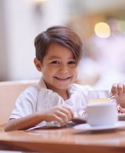 Niño feliz desayunando en un restaurante, sentado a la mesa con comida y bebidas.