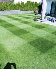 Gepflegter Rasen mit Streifenmuster vor einer Terrasse mit Tisch und Stühlen, im Garten einer Wohnung.