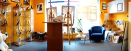 Ein Kunstgeschäft mit orangefarbenen Wänden, Bildern, Staffeleien und einem blauen Sessel.