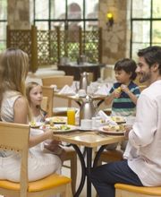 Familia comiendo en un restaurante, sentados en una mesa con platos y bebidas alrededor.