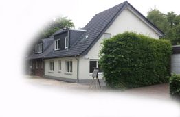 Weiße Doppelhaushälfte mit grauem Dach und einer großen Hecke auf der rechten Seite.