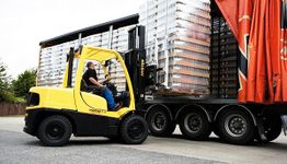 Montacargas amarillo cargando palés en un camión con lona roja en un área de carga.