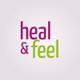 Textlogo mit den Worten "heal & feel" in lila und grün auf grauem Hintergrund.