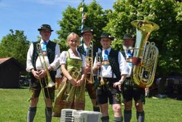 Eine Blaskapelle in traditioneller bayerischer Tracht steht auf einer Wiese.