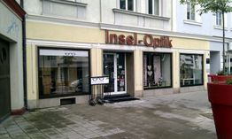 Optikergeschäft "Insel-Optik" mit Schaufenstern und Blumenkübel vor dem Eingang.