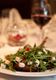 Plate of arugula salad with cheese cubes, wine glass in blurred background.