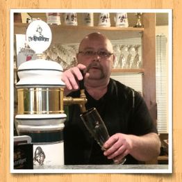 Mann zapft Bier an der Theke, umgeben von Bierkrügen und Gläsern im Hintergrund.