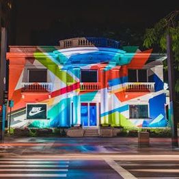 Fachada iluminada de prédio com arte colorida e logo da Nike à noite.
