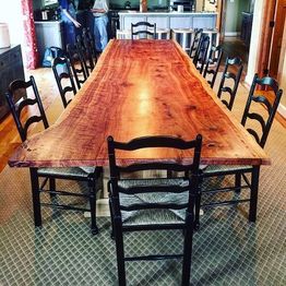 Long wooden dining table with natural edges, surrounded by black chairs on a patterned carpet.