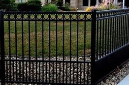 Black metal fence with circular patterns, surrounding a grassy yard with a rocky border.