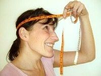 Frau misst ihren Kopfumfang mit einem Maßband und lächelt.