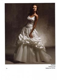 Frau in einem eleganten, weißen, voluminösen Kleid mit Rüschen, posiert vor dunklem Hintergrund.