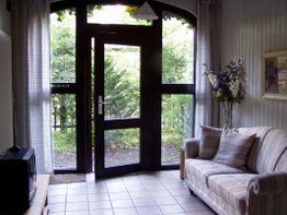 Helles Wohnzimmer mit Sofa und großem Fenster. Blick auf grünen Garten durch Glastür und Fenster.