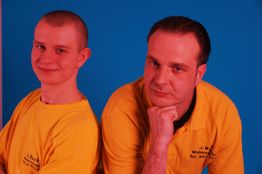 Zwei Männer in gelben Shirts vor blauem Hintergrund, einer lächelt, der andere stützt sein Kinn.