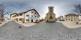 Panoramablick auf einen Platz mit Kopfsteinpflaster, Kirche und umgebenden Gebäuden.