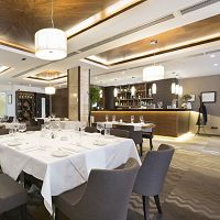 Elegant restaurant interior with a neatly set table, modern decor, and a well-lit bar area.