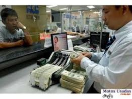 Empleado bancario contando billetes, mientras un cliente mira desde el otro lado del mostrador.