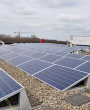 Paneles solares en un techo plano, cielo parcialmente nublado, grúa y árboles al fondo.