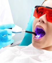 Dentista usando luz LED en paciente con gafas rojas en consulta dental.