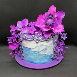 Künstlerische Torte mit lila Blumen und dekorativen Details vor schwarzem Hintergrund.