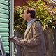 Person inspecting a house exterior with a clipboard, next to a green wall and garden.