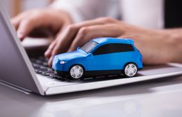A blue toy car on a laptop keyboard with hands typing in the background.
