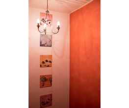 Flur mit Kronleuchter, oranger Wand und vier quadratischen Bildern in verschiedenen Farben.