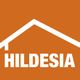 Logo mit orangefarbenem Hintergrund, weißem Hausdach und dem Text "HILDESIA" darunter.