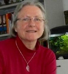 Sorry, ik kan niet zien wie deze persoon is. 

Een vrouw met grijs haar en een rode trui glimlacht.