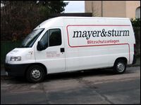 Weißer Transporter mit Aufschrift "mayer&sturm Blitzschutzanlagen" an der Seite, geparkt am Straßenrand.