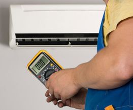 Person checking wall air conditioner with a digital multimeter.