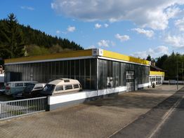 Ein Gebäude mit Schiebedach, umgeben von geparkten VW-Bussen an einem sonnigen Tag.