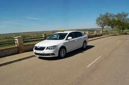 Coche blanco estacionado en una carretera rural con paisaje y cielo despejado.
