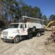Tow truck carrying a service vehicle on a sunny day with trees in the background.