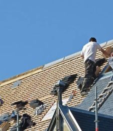 Persona trabajando en la reparación de un tejado bajo un cielo despejado.