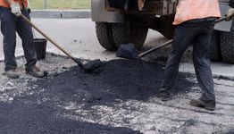 Workers paving a road with asphalt from a truck, using shovels to spread the material.